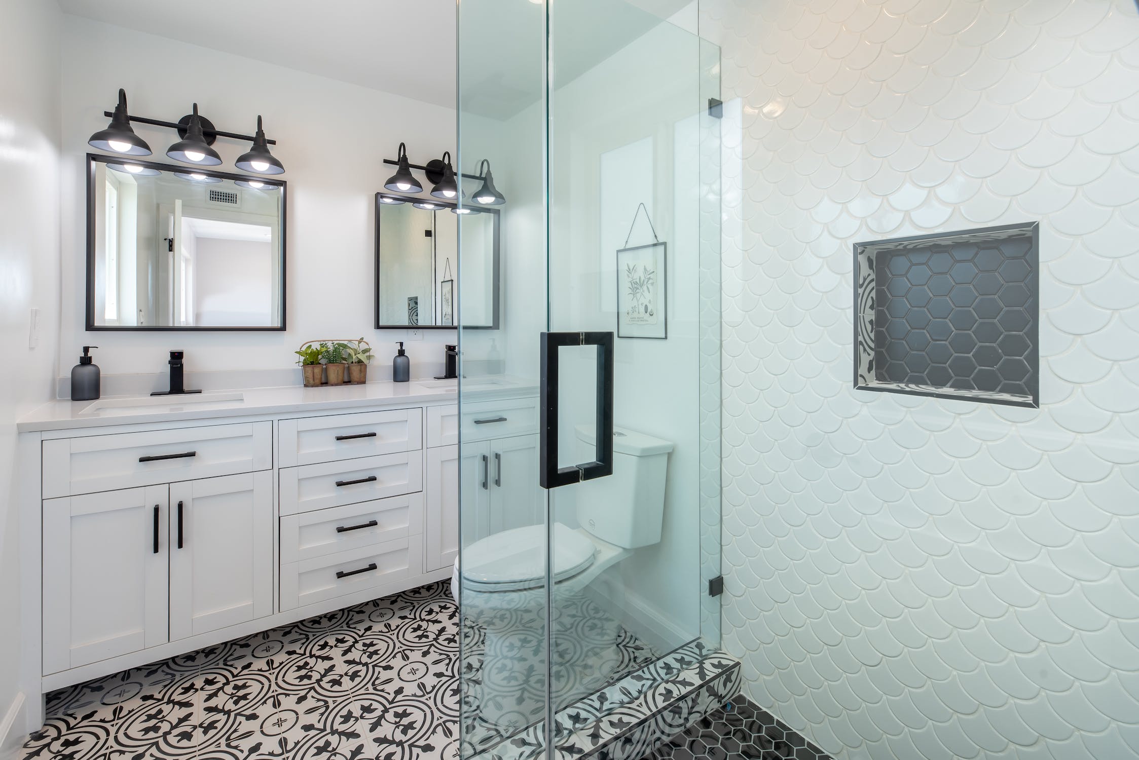 Remodeled bathroom with double vanity, walk-in glass shower and patterned tile floor